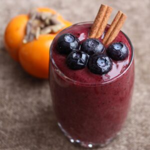 pretty smoothie with blueberries on top and a persimmon in the back