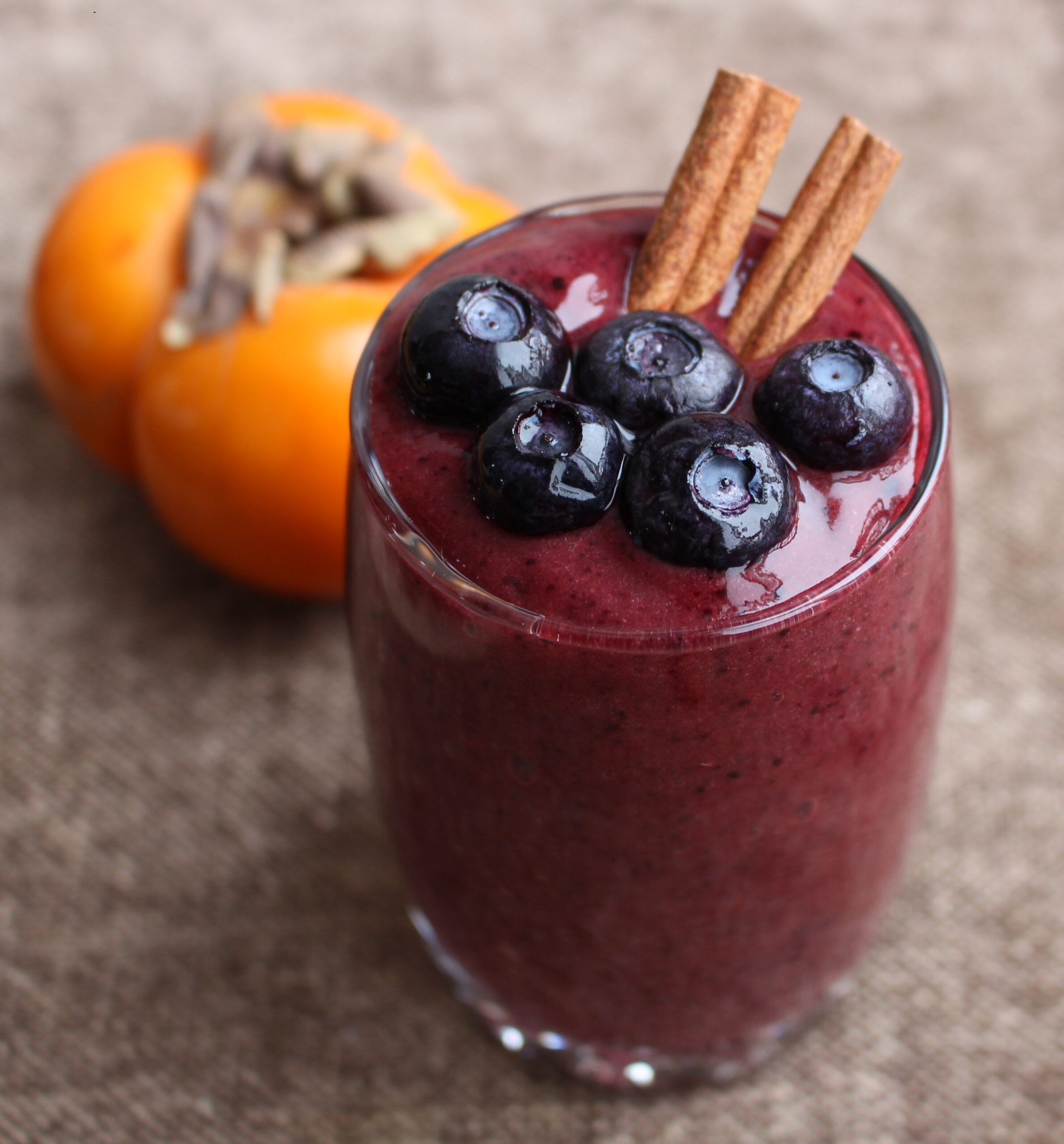 pretty smoothie with blueberries on top and a persimmon in the back