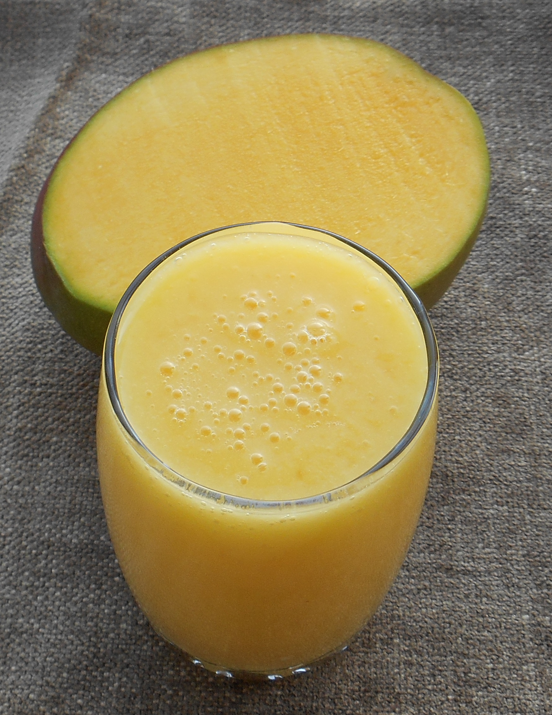 simple orange color smoothie cup with a mango behind it