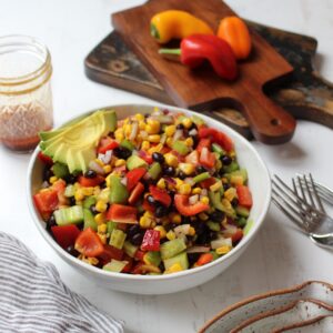 mexican salad in a bowl with vinaigrette on the left and fork on the right