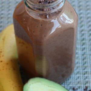 tall glass with chocolate smoothie with and avocado and a banana on the side