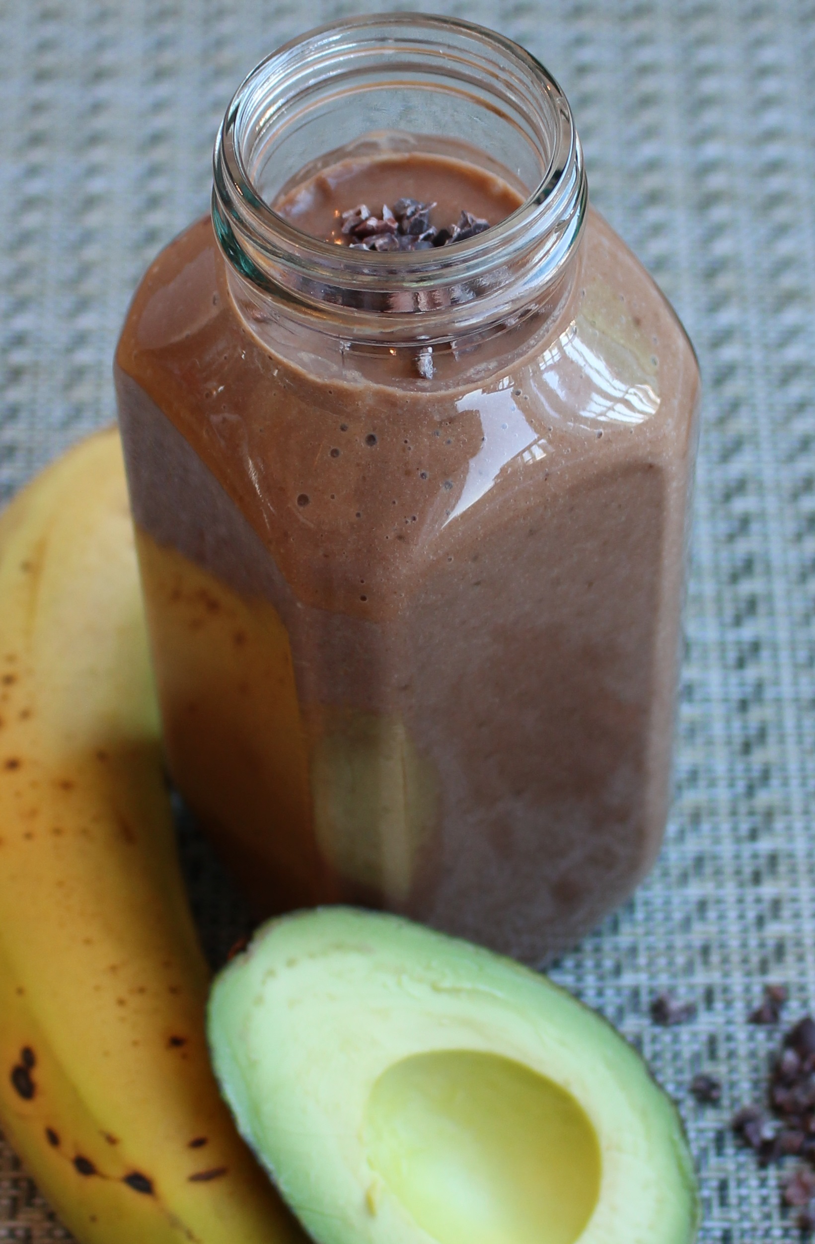 tall glass with chocolate smoothie with and avocado and a banana on the side