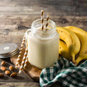 creamy beige smoothie with banana next to it and a straw
