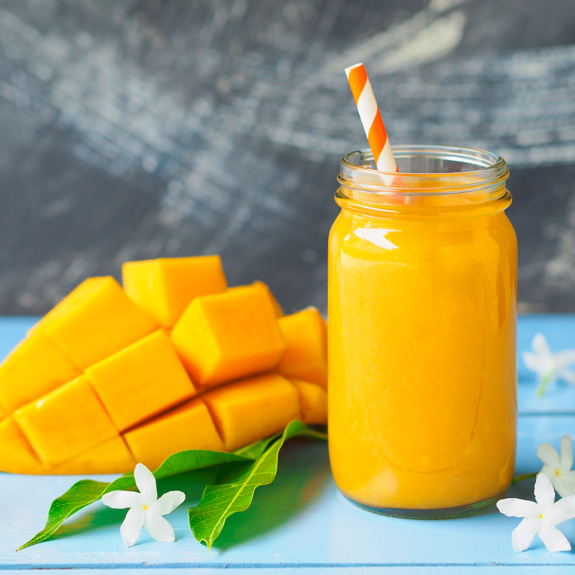 orange looking smoothie with a mango on the side with a straw