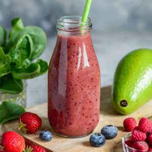 a purple/pink smoothie with berries and avocado around it