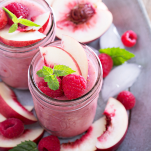 pink raspberry/peach smoothie with fruits around it