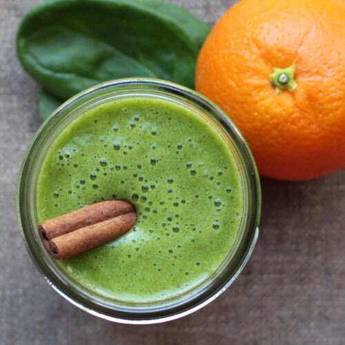 green smoothie with cinnamon on top. Orange and spinach beside.