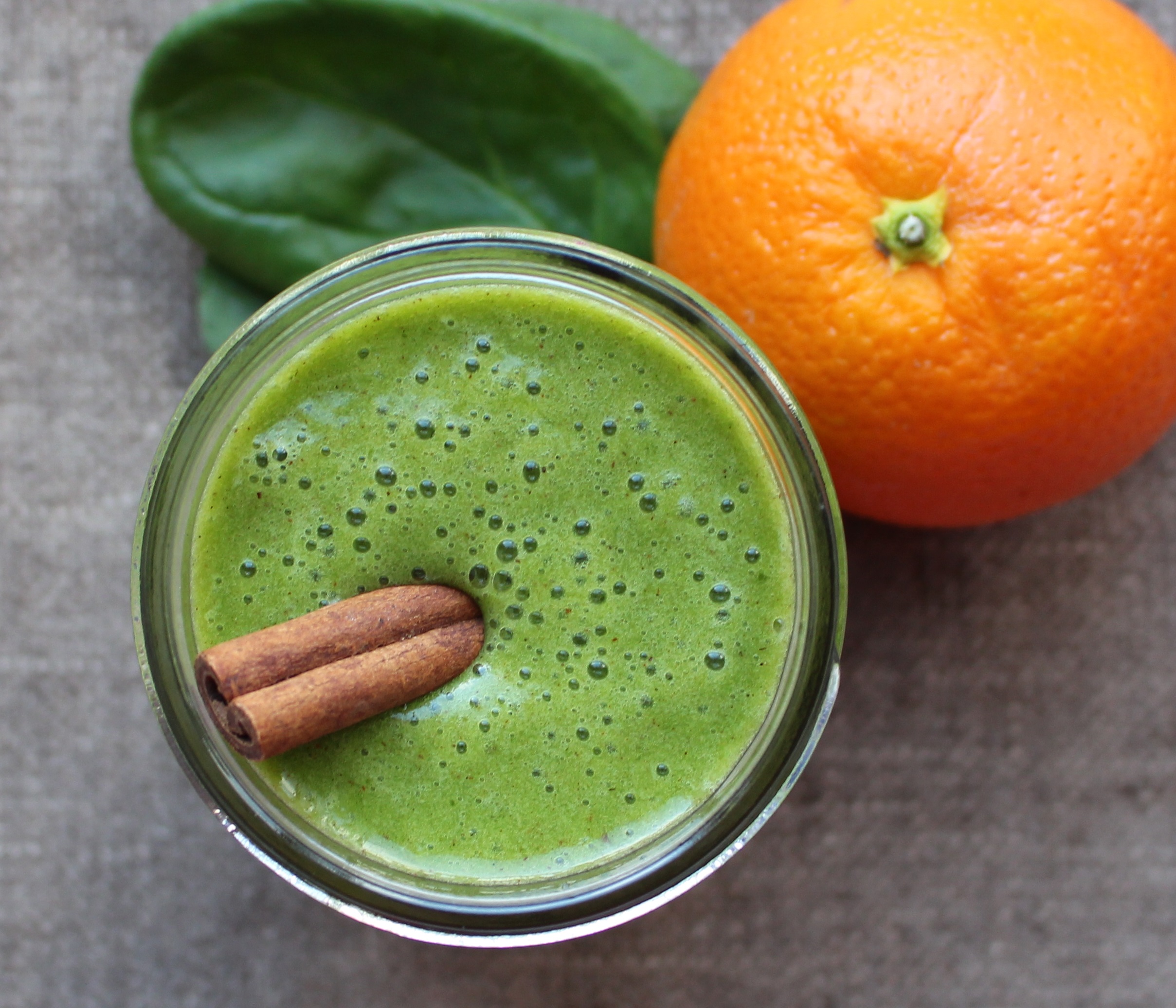 green smoothie with cinnamon on top. Orange and spinach beside.