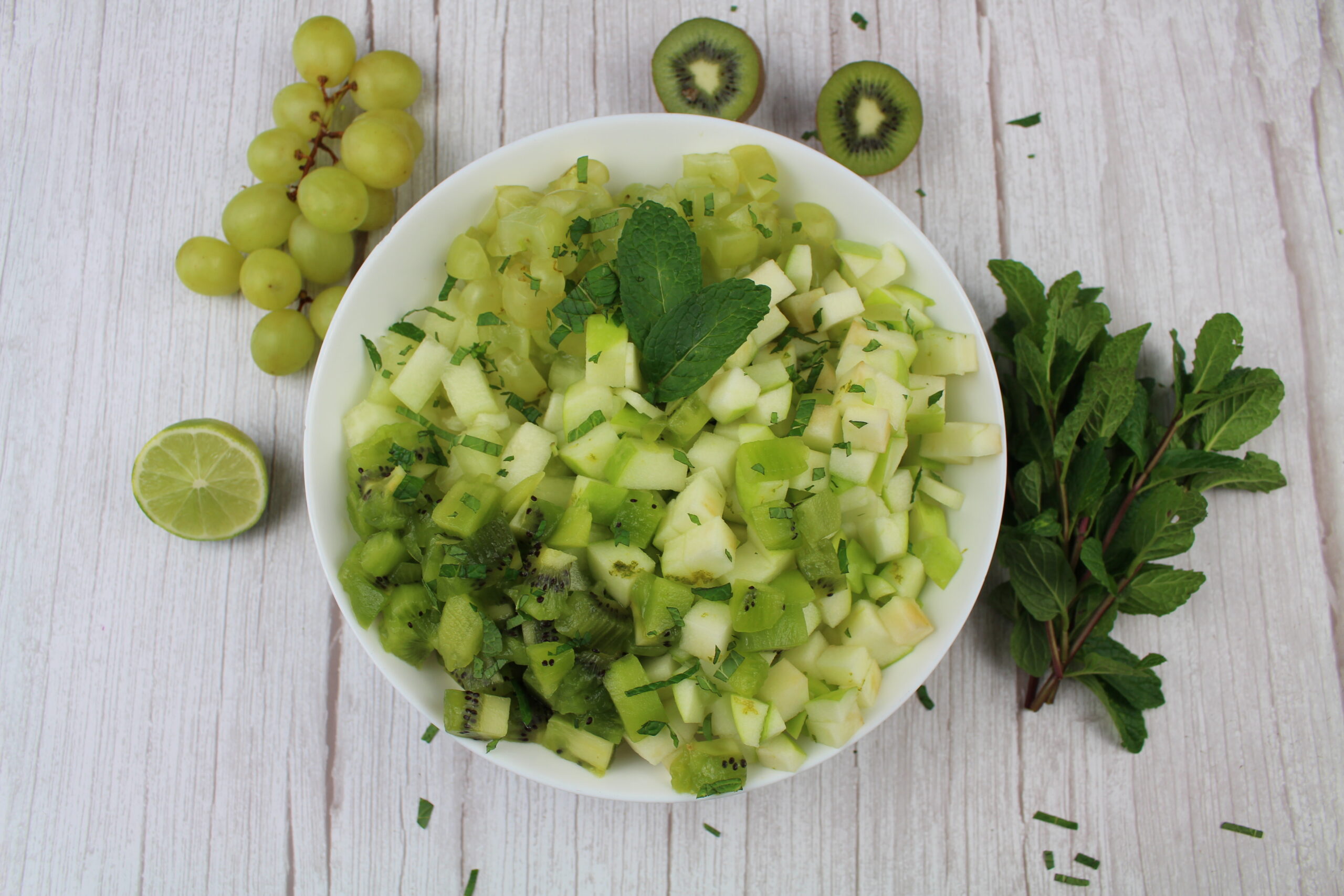 bowl of green fruit salad from the top with mint on the side