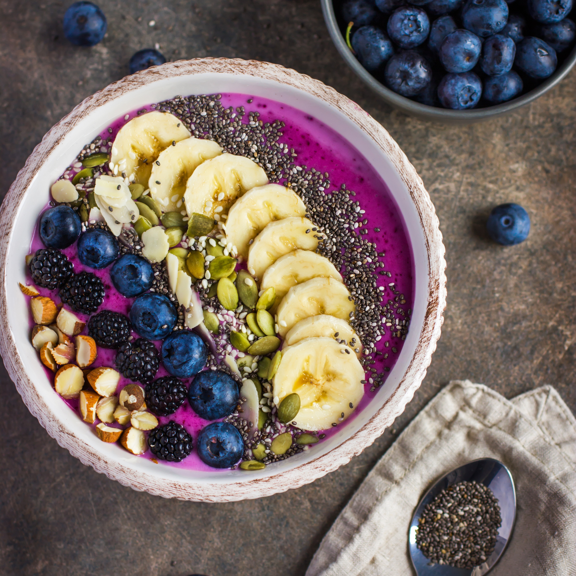 Blueberry smoothie bowl with babana slices on top and slivered almonds and chia seeds