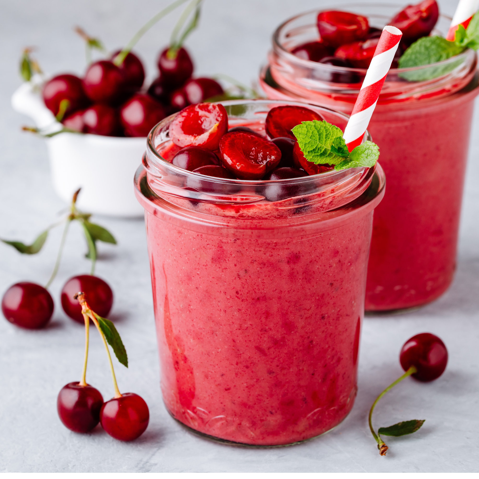 cherry smoothie with a straw in it and cherries around cup