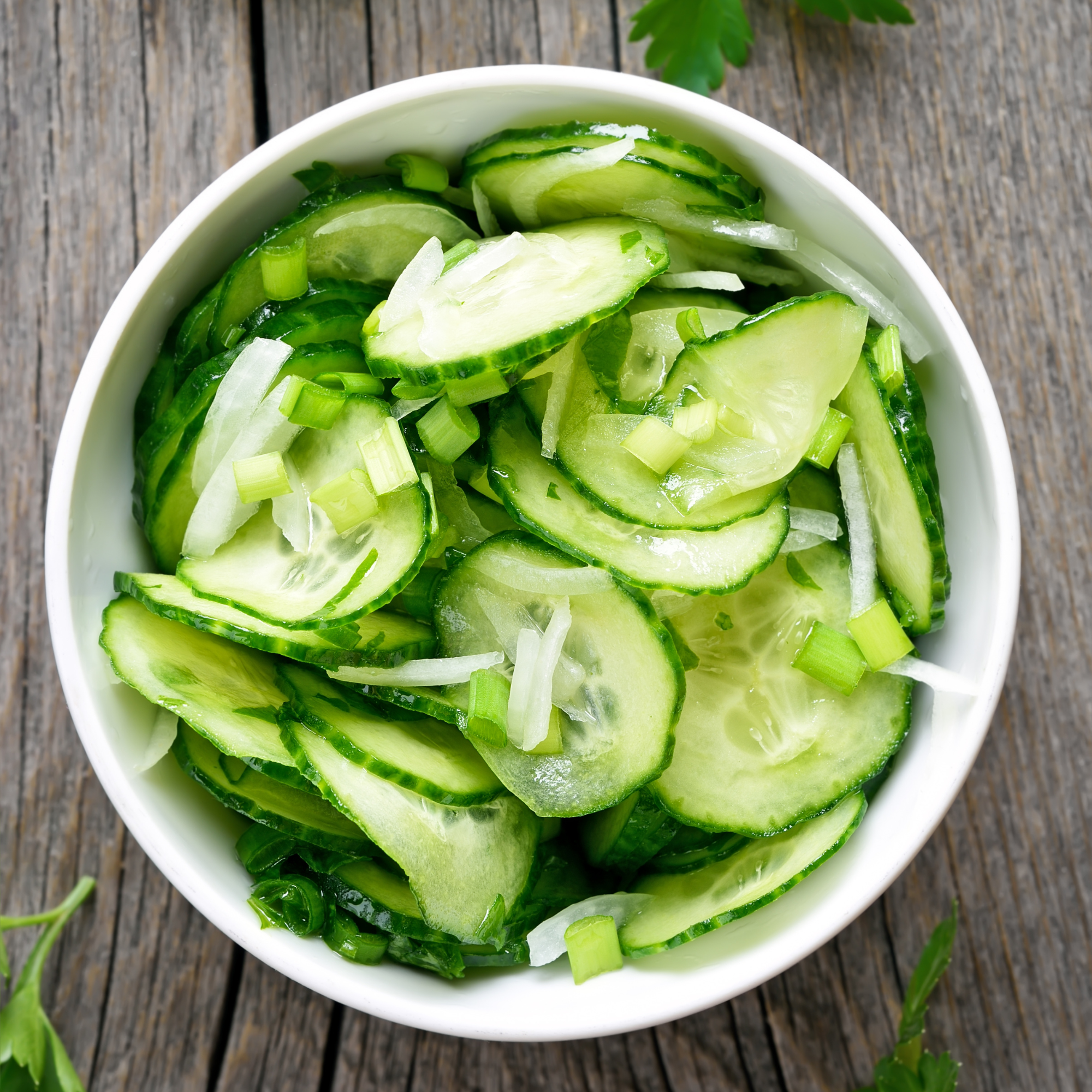 simple cucumber salad in a bowl with fresh parsley around it