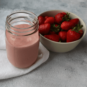 Vegan Strawberry cashew milkshake with bowl of strawberries