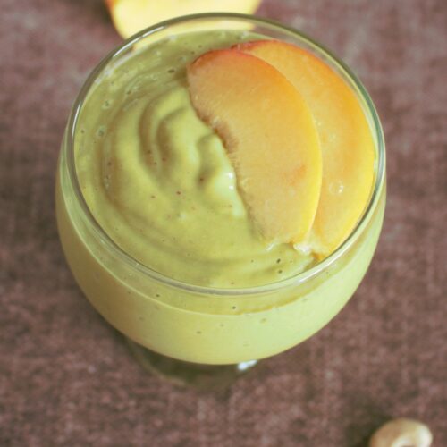 green smoothie with peaches on top and cashews