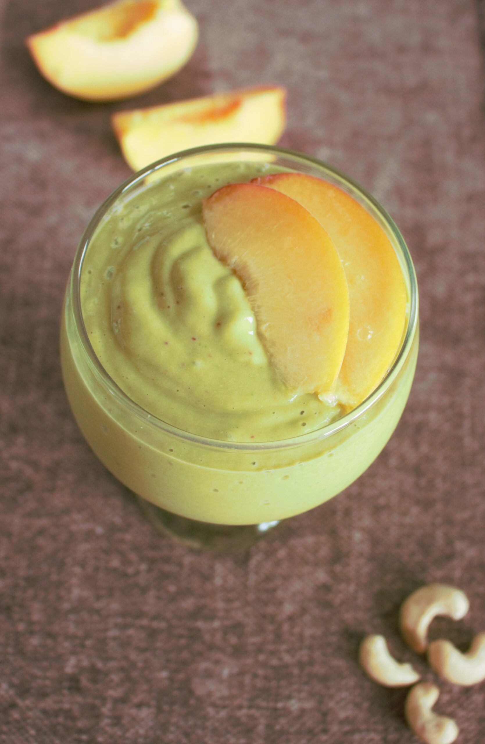 green smoothie with peaches on top and cashews