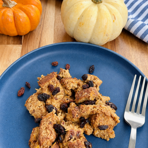 Homemade pumpkin bread pudding in a blue plate with raisins and pumpkin all around