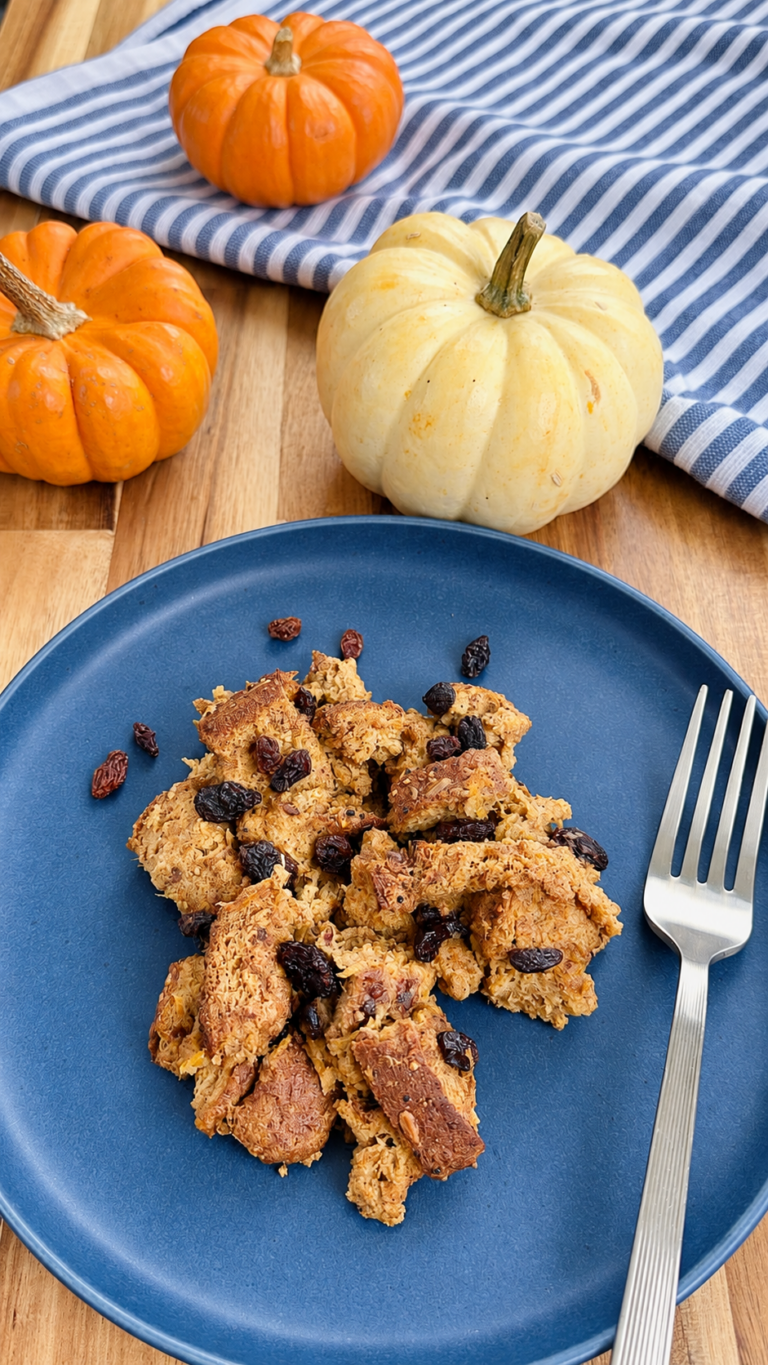 Homemade pumpkin bread pudding in a blue plate with raisins and pumpkin all around