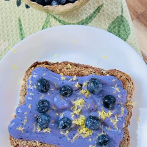 a toast with blueberry cream and zest on top with a blueberry bowl on the side