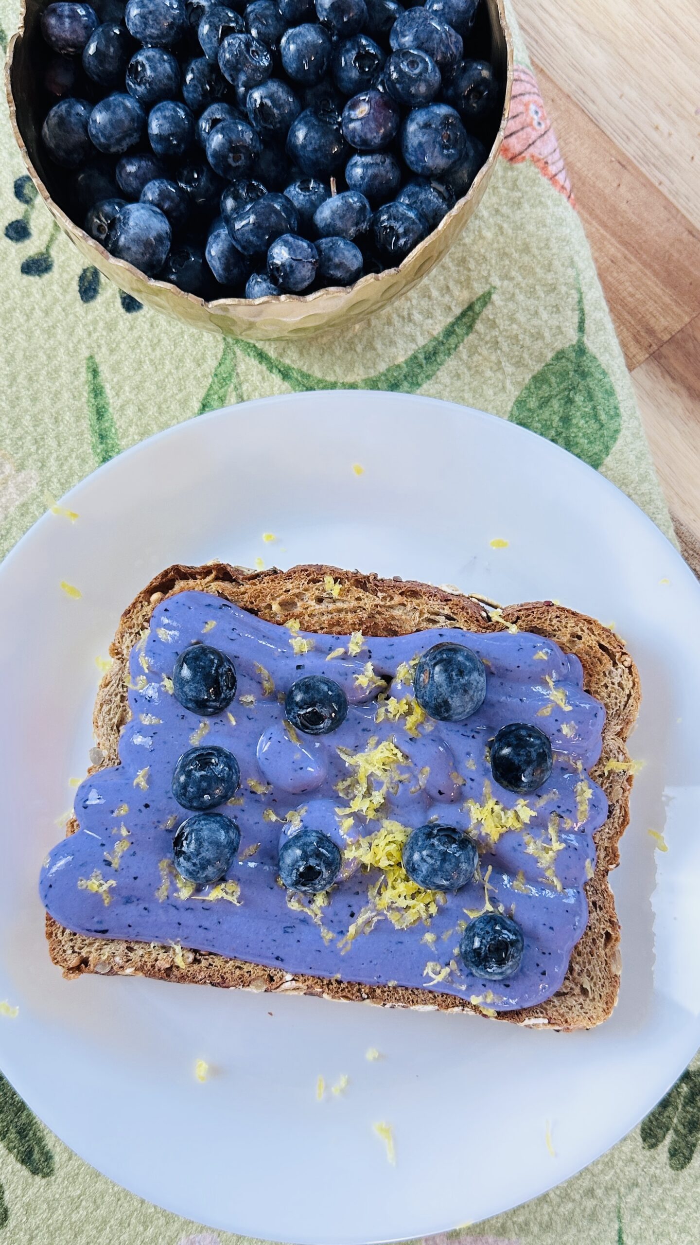 a toast with blueberry cream and zest on top with a blueberry bowl on the side