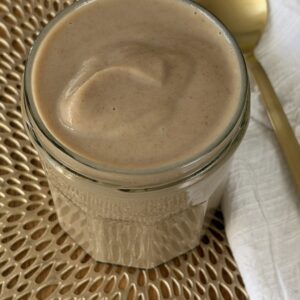 Jar of creamy date paste on a nice gold mat next to a white cloth and gold spoon