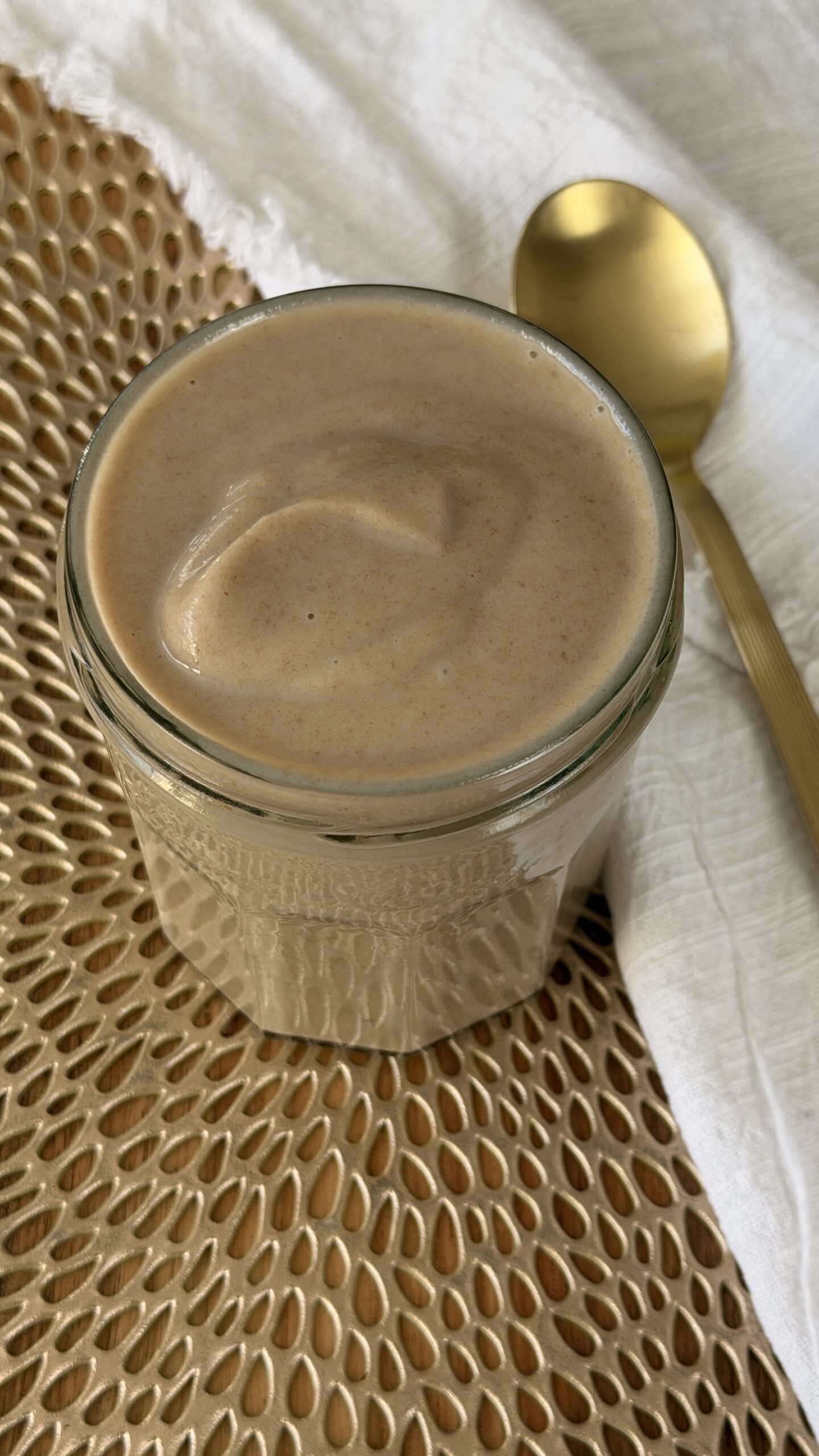 Jar of creamy date paste on a nice gold mat next to a white cloth and gold spoon